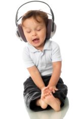 Picture of cute toddler girl, white shirt and jeans, wearing music headphones, singing holding her toes