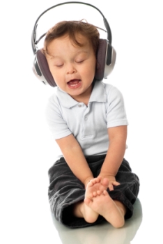 Picture of cute toddler girl, white shirt and jeans, wearing music headphones, singing holding her toes