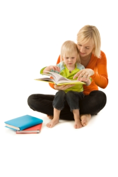 Photo of a mother reading with her blonde toddler son with other books on the floor.