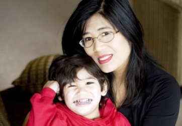 Cute picture of baby with cerebral palsy using baby sign language while sitting on moms lap